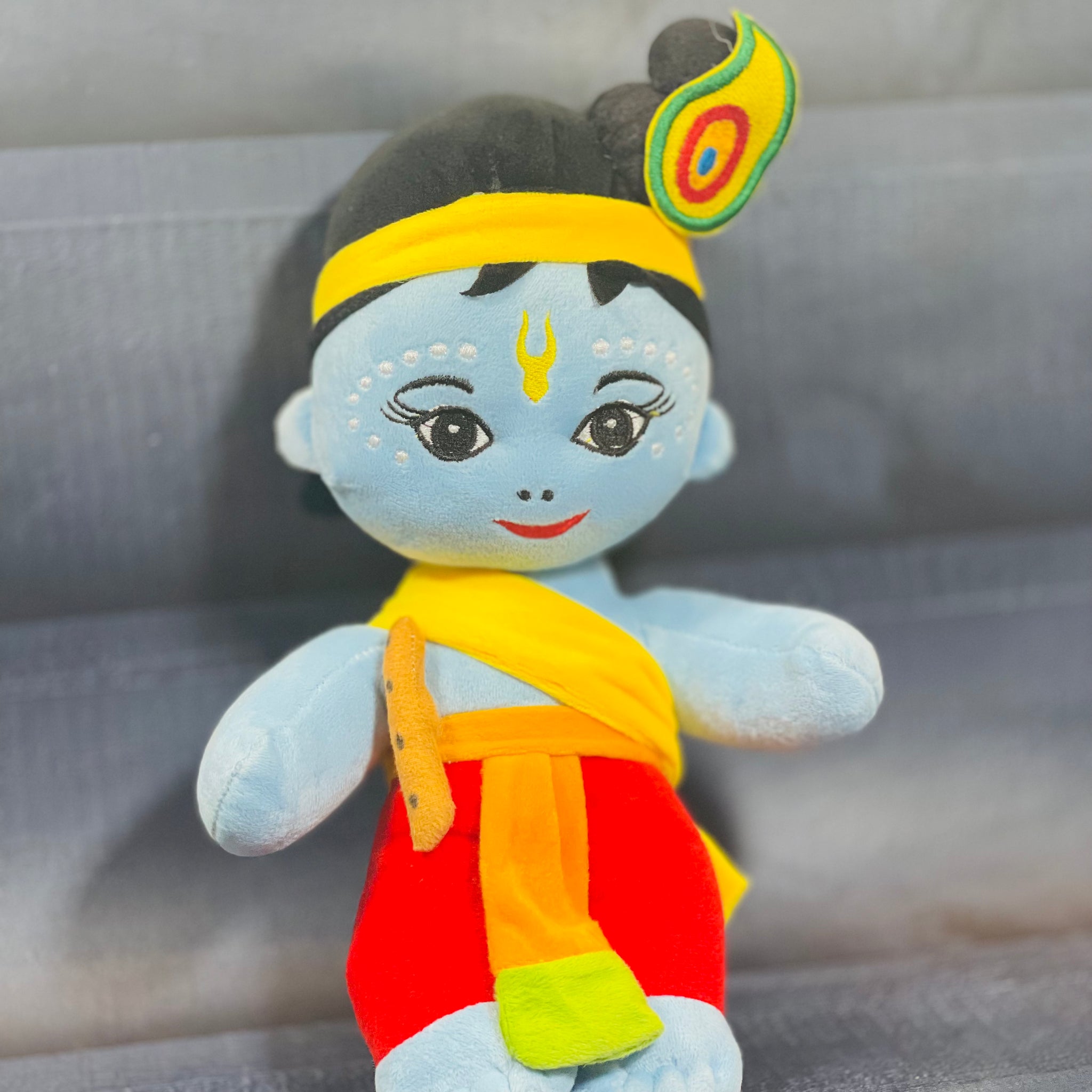 Soft plush toy of Little Krishna with blue skin, yellow dhoti, and peacock feather crown, perfect for devotional gifting and children’s play.